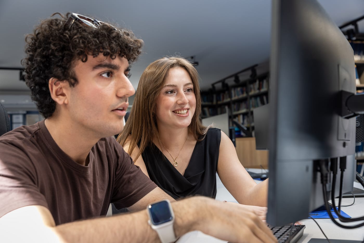 Dva studenti pracují společně u počítače v univerzitní knihovně na UNYP.